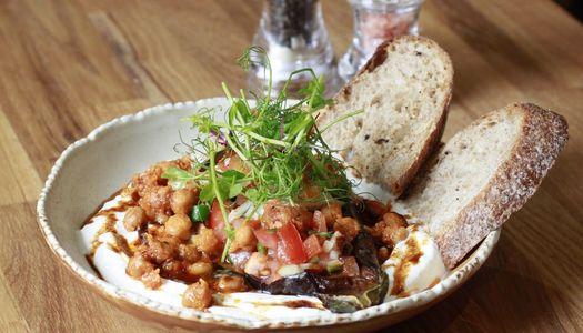 A Mediterranean-style brunch dish with chickpeas, tomatoes and herbs served over creamy yoghurt, with slices of rustic sourdough bread. Turkish influences