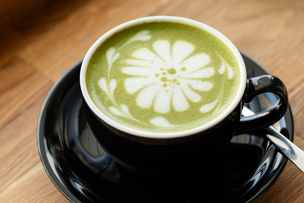 Green frothy matcha latte with flower latte art in a black mug. Headlining image to our Matcha Brighton guide