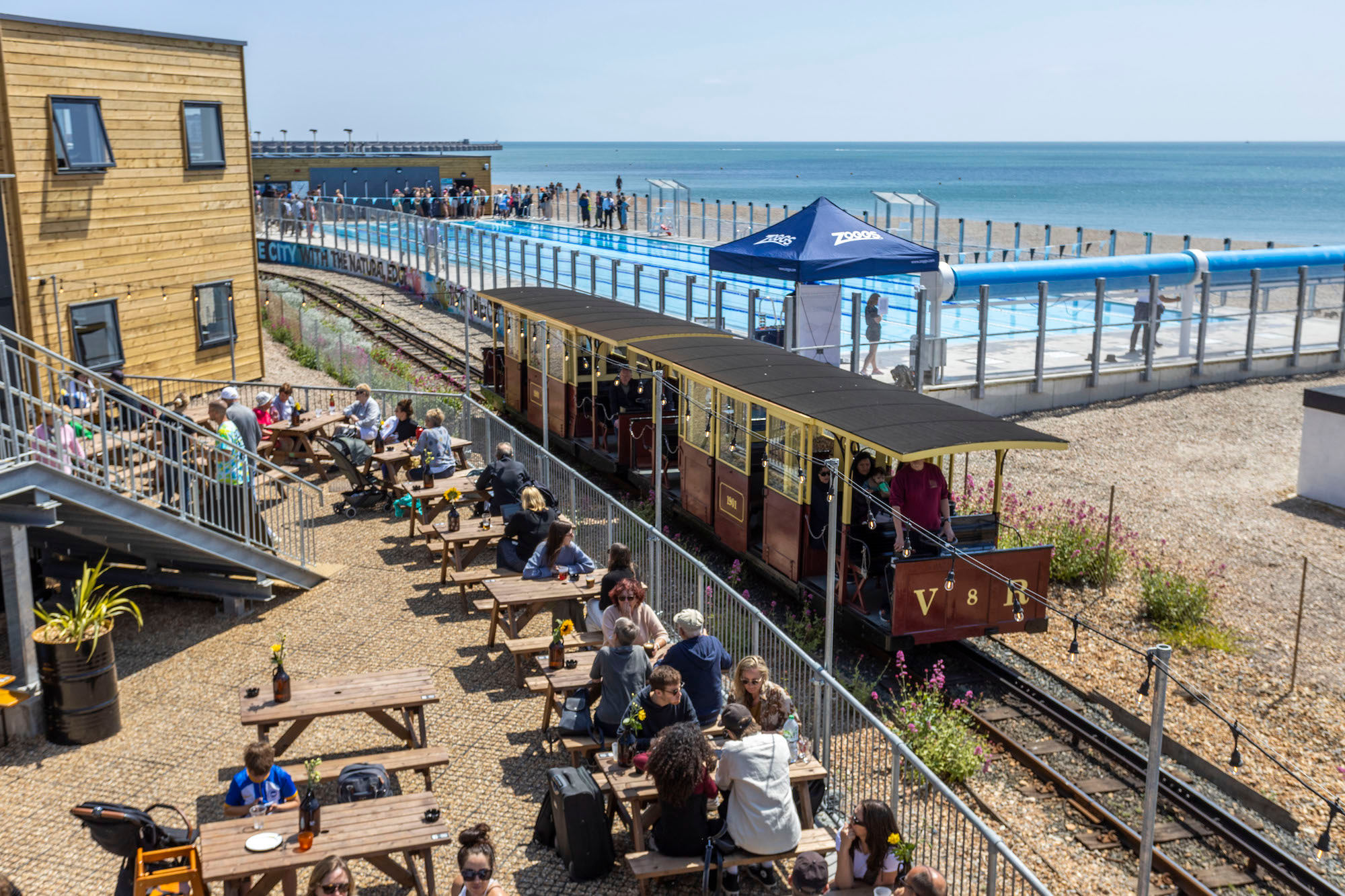 The Volks railway runs through the site where swimmers enjoy the opening day of Sea Lanes - the UK's first National Open Water Swimming Centre . At the heart of Sea Lanes Brighton is a 50m 6 lane outdoor pool located on the beach with local fitness, wellbeing, food, and beverage businesses creating a hub of units from sun up to sundown on the seafront in Kemp Town, Brighton ***Pic by David McHugh / Brighton Pictures 07768 721637***