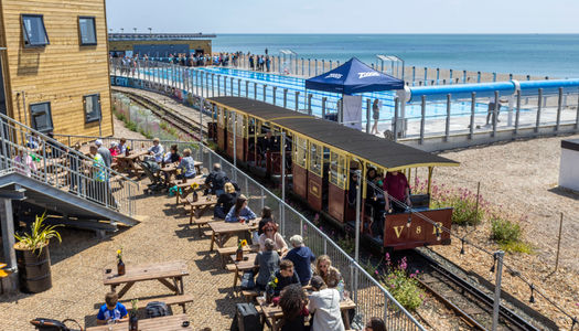 The Volks railway runs through the site where swimmers enjoy the opening day of Sea Lanes - the UK's first National Open Water Swimming Centre . At the heart of Sea Lanes Brighton is a 50m 6 lane outdoor pool located on the beach with local fitness, wellbeing, food, and beverage businesses creating a hub of units from sun up to sundown on the seafront in Kemp Town, Brighton ***Pic by David McHugh / Brighton Pictures 07768 721637***
