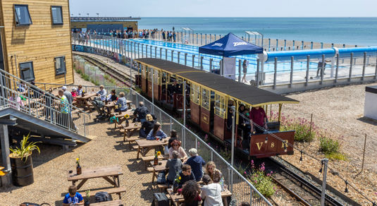 The Volks railway runs through the site where swimmers enjoy the opening day of Sea Lanes - the UK's first National Open Water Swimming Centre . At the heart of Sea Lanes Brighton is a 50m 6 lane outdoor pool located on the beach with local fitness, wellbeing, food, and beverage businesses creating a hub of units from sun up to sundown on the seafront in Kemp Town, Brighton ***Pic by David McHugh / Brighton Pictures 07768 721637***