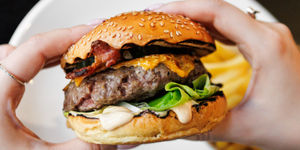 Hands holding The North Star Burger in Brighton. A large single pattie, seeded bun, lettuce. Gastro pub burger, served with chunky chips. Located opposite The Royal Pavilion.