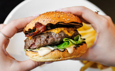 Hands holding The North Star Burger in Brighton. A large single pattie, seeded bun, lettuce. Gastro pub burger, served with chunky chips. Located opposite The Royal Pavilion.