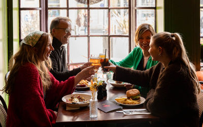group of friends sitting at the table next to window and enjoying food and drink