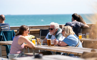 Guests enjoying a pint at Sea Lanes. 3 People drinking craft beer with views of teh sea in the background