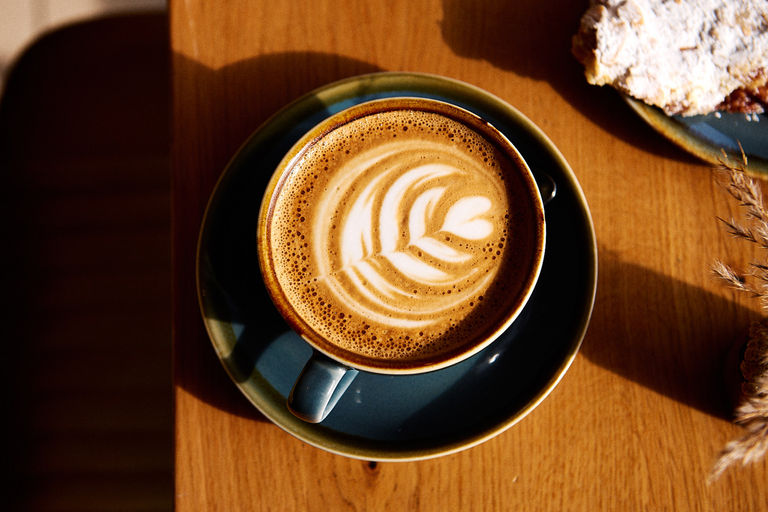 Overhead of a latte with an almond croissant and sun shining