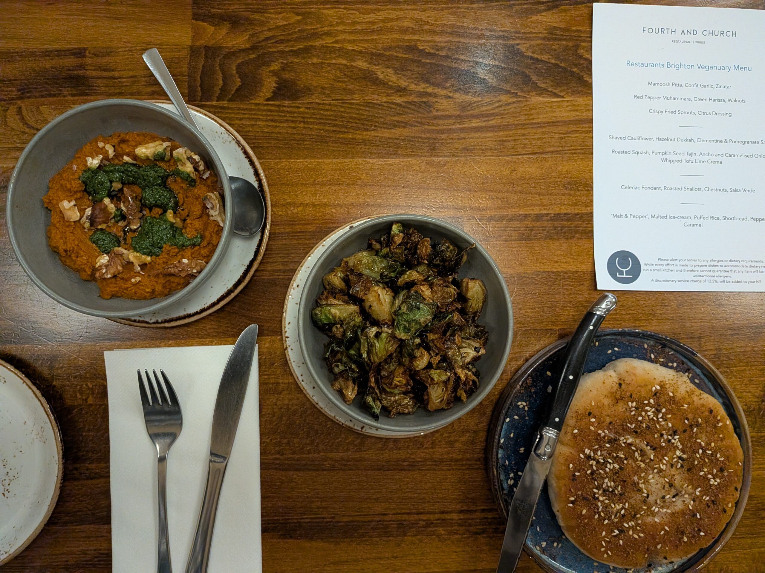 over head shot of mamoosh pitta with confit garlic and za’atar, alongside some red pepper muhammara with green harissa and walnuts and crispy fried sprouts in citrus dressing