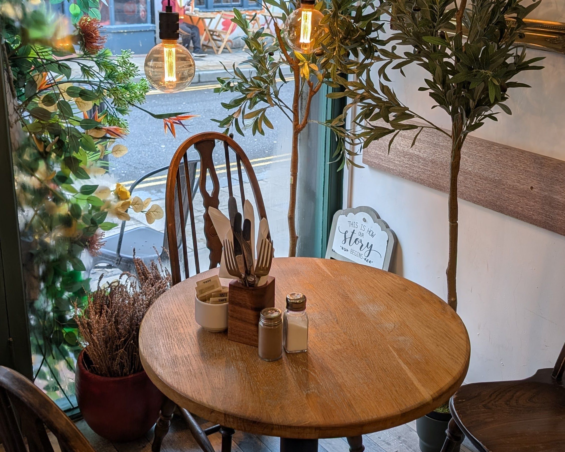 Cosy window table inside Meo Brighton in Kemptown, with warm lighting, wooden furniture and leafy décor.