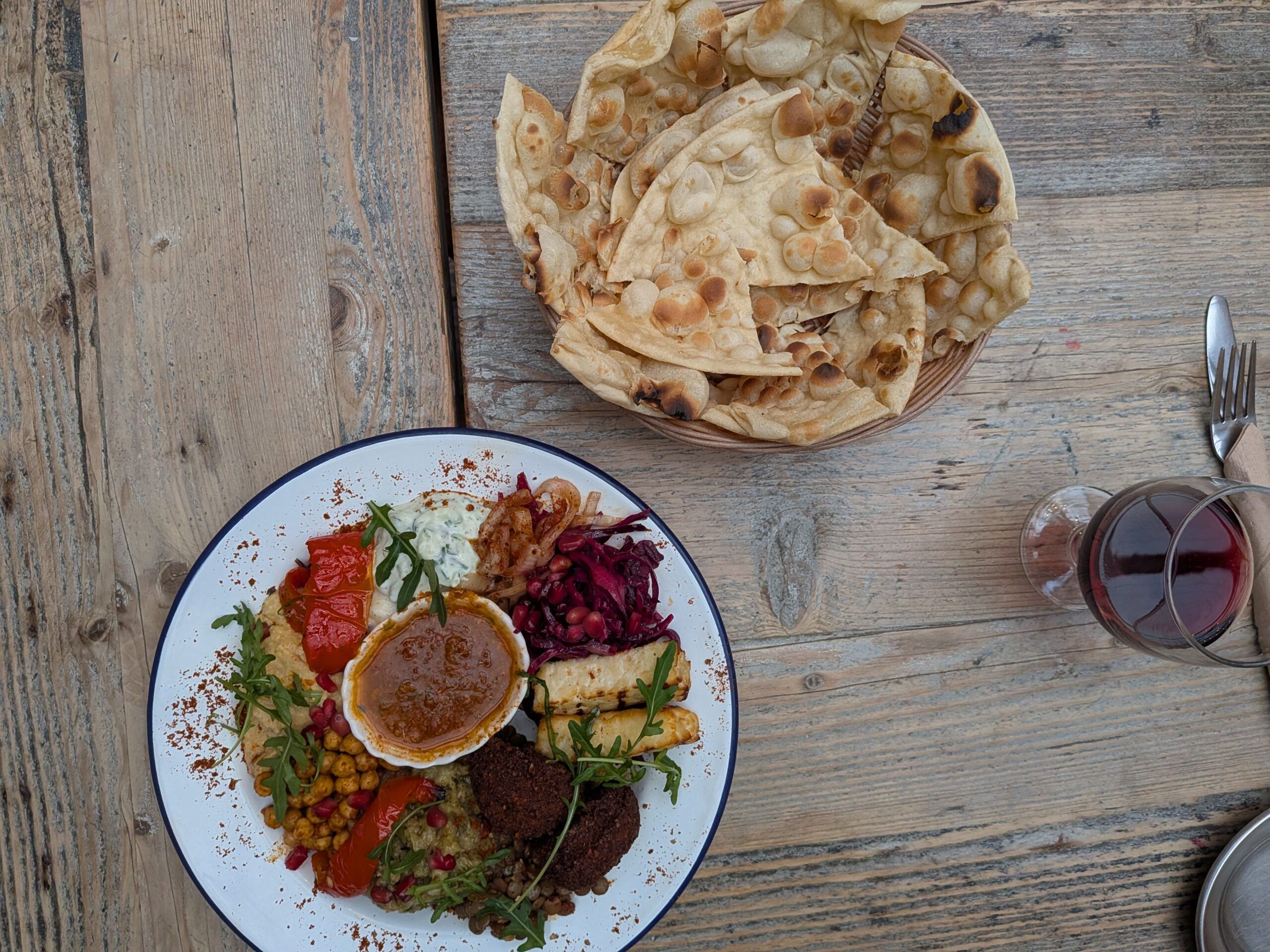 Middle Eastern cousine at Lavash, mezze platter with falafel, grilled halloumi, hummus, pickles and flatbread, served with a glass of red wine.
