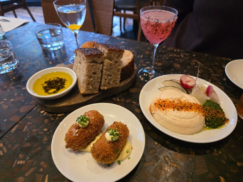three startes on the table including croquettes, bread, olive oil, hummous