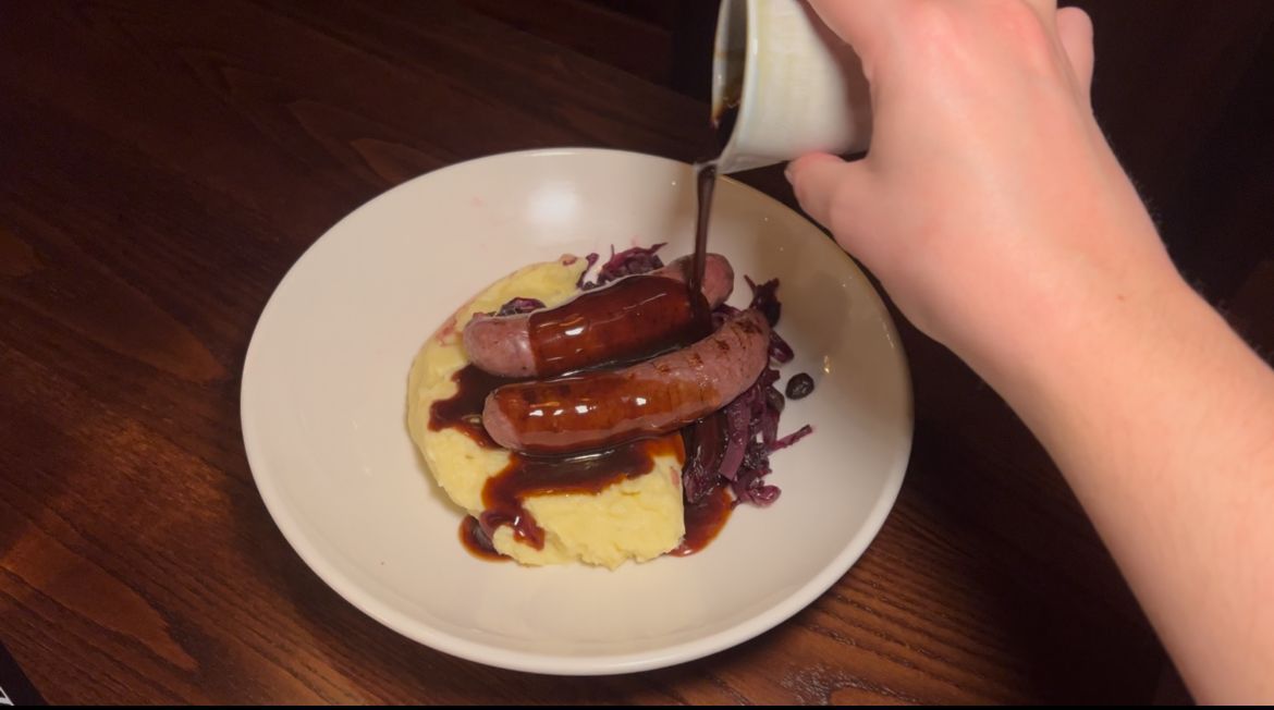 shallot gravy being poured over mashed potates and sauseges