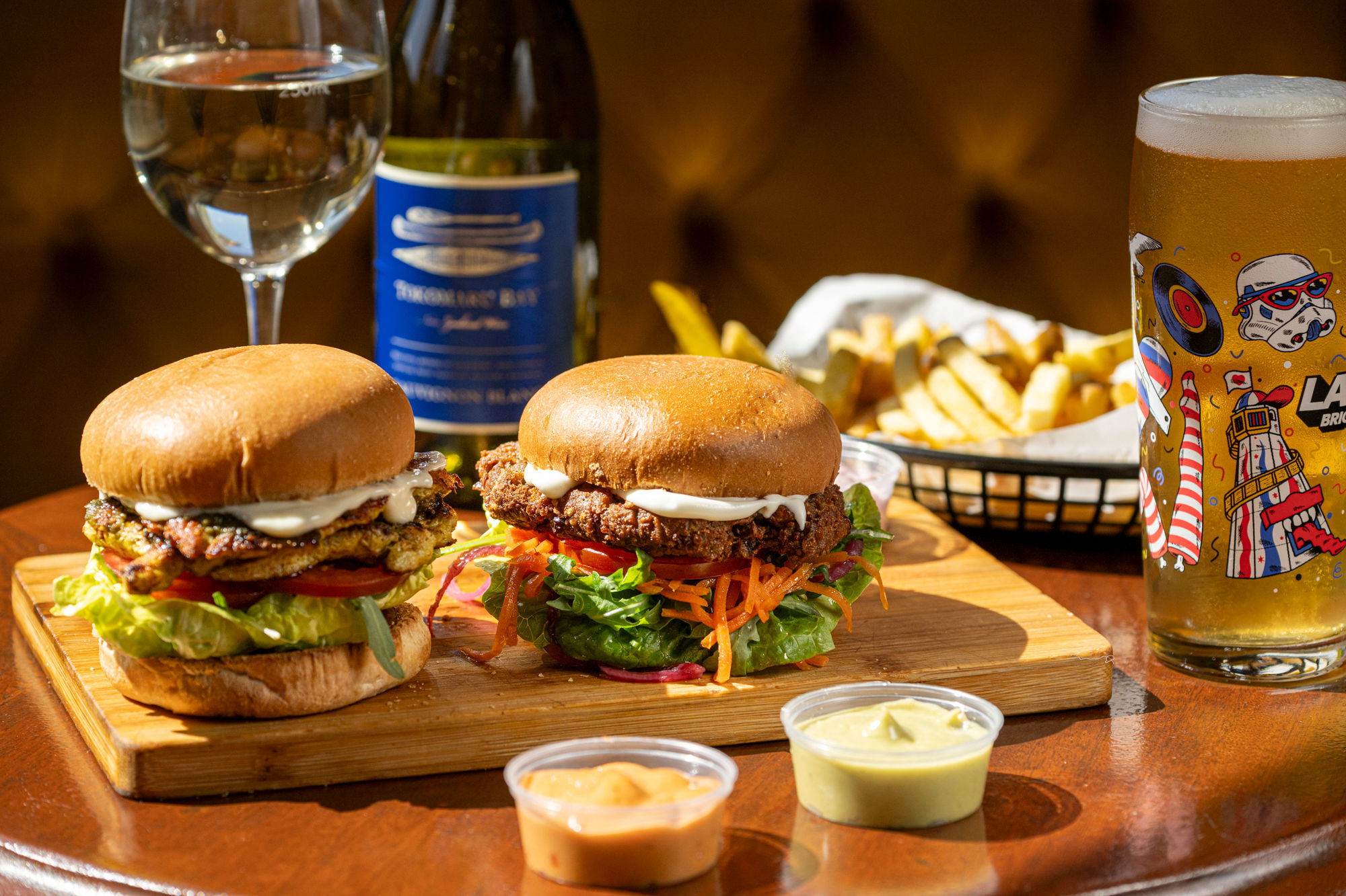 two burgers on the wooden platter served with sauces and beer