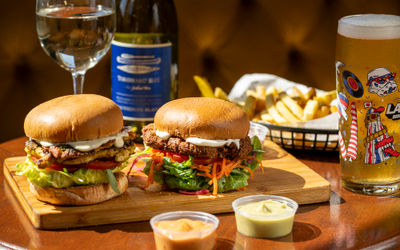 two burgers on the wooden platter served with sauces and beer