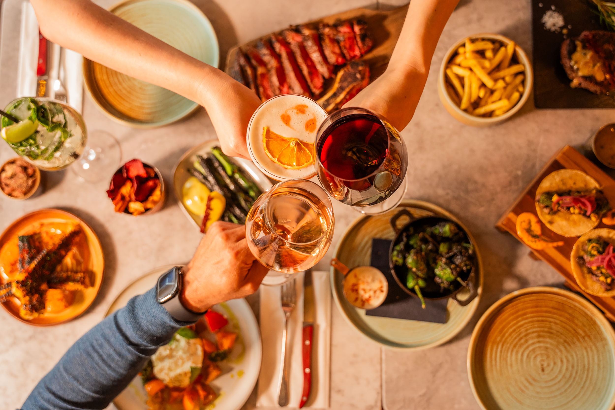 over head shot of the table at Kindling and people having a toast with their drinks above food
