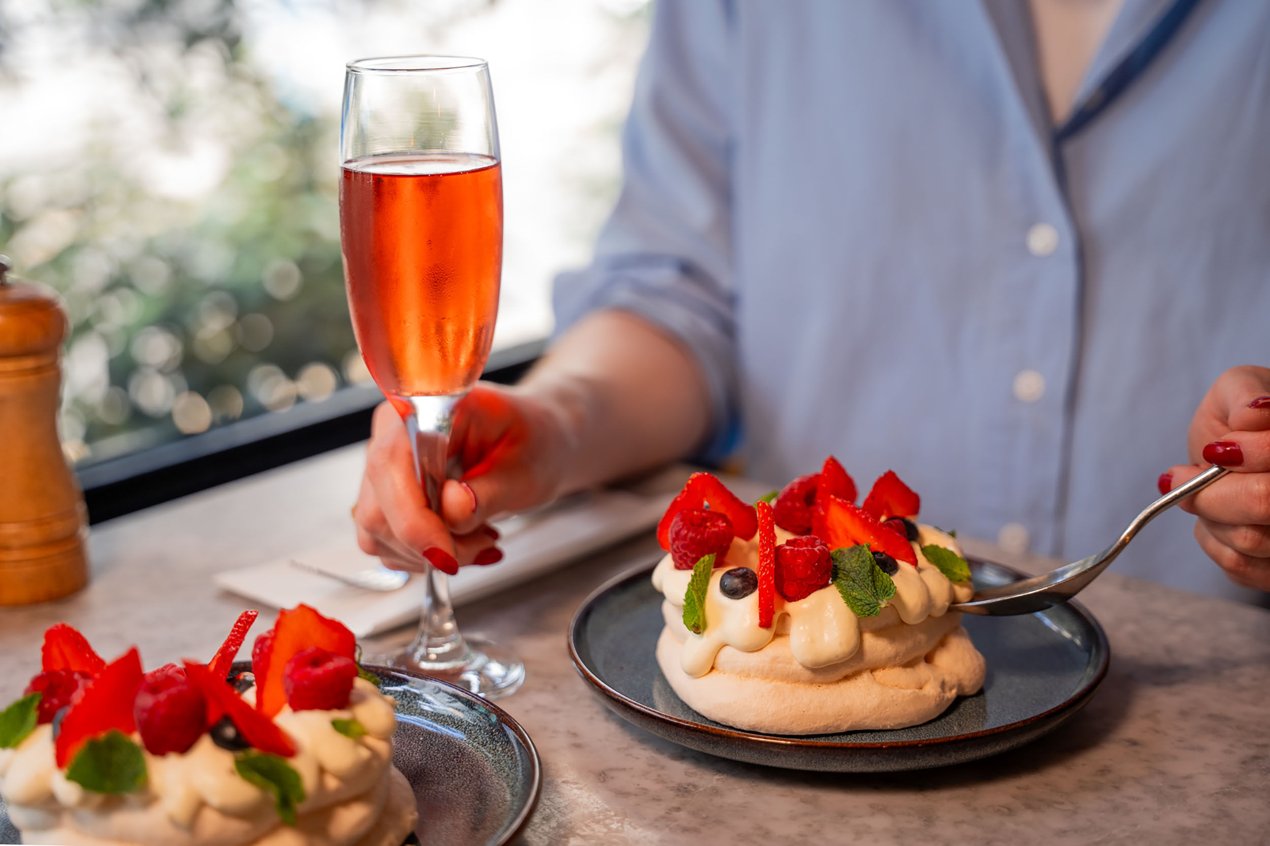 person holding glass of sparkling next to their dessert