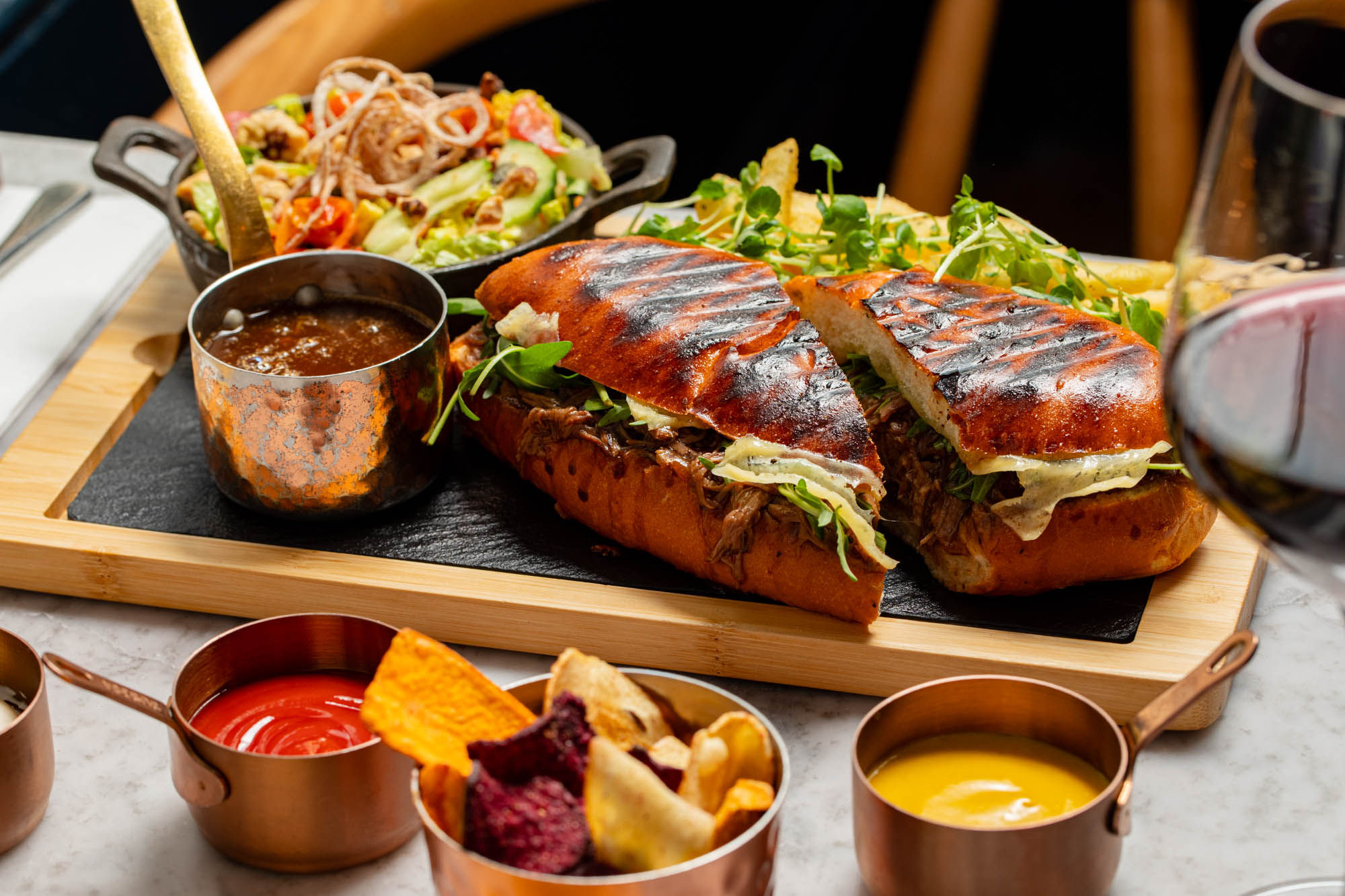 side shot of the burger cut in a half and served with chips and sauces