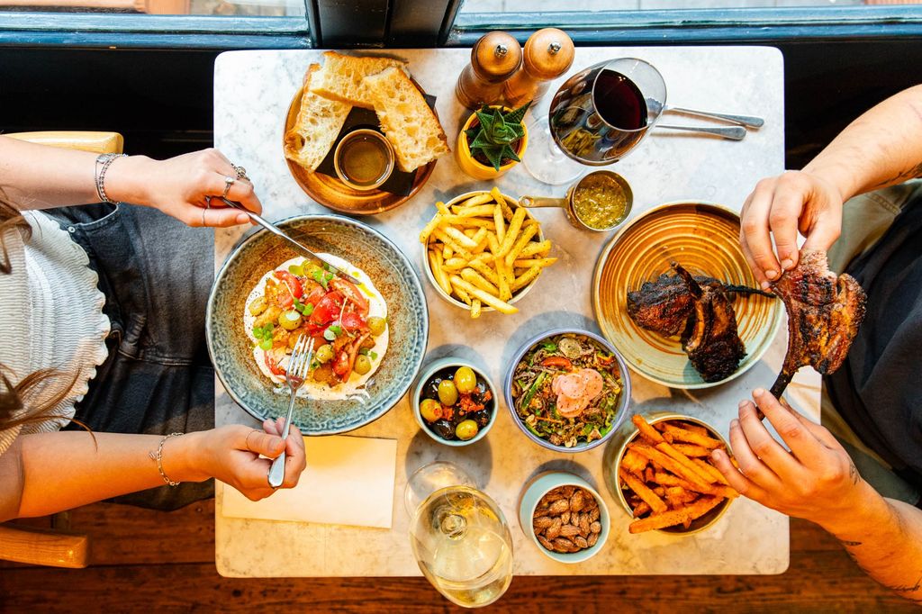 A top shots of a 2 person table full of food and drinks. With 2 diners tucking in to their food.