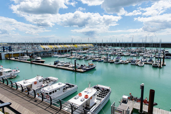 Brighton Marina. Several boats sit in the marina with the harbour wall behind. It's a sunny day with big white clouds.