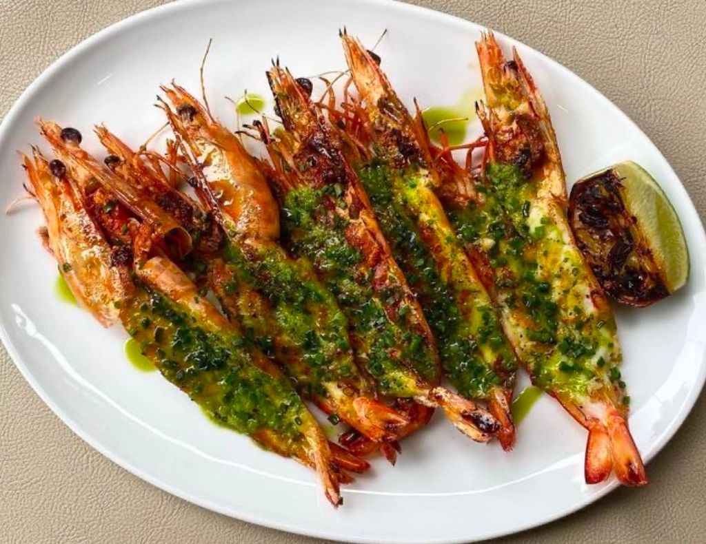 Large prawns lined up on a plate with a fresh herb sauce 