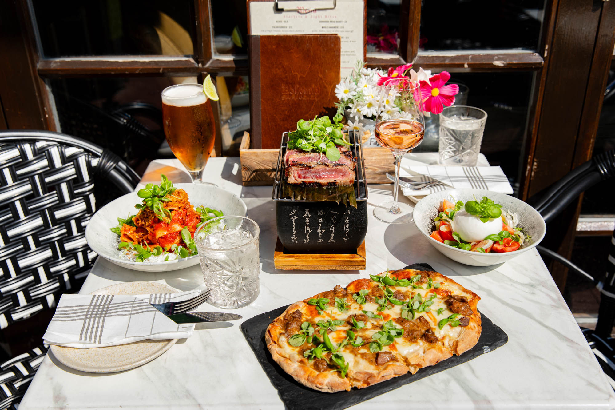 side shot of the table laid out with couple of dishes including pizza, burrata salad and spaggethi served with drinks