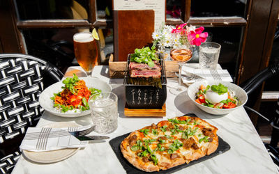 side shot of the table laid out with couple of dishes including pizza, burrata salad and spaggethi served with drinks