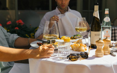 Two men alfresco dining on a sunny day with glasses of white wine and a table of Italian food.