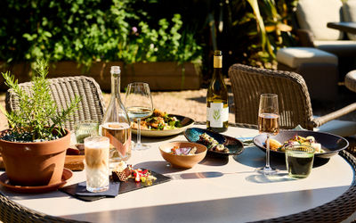 An alfresco summer feast with wine on the terrace with foliage in the background.
