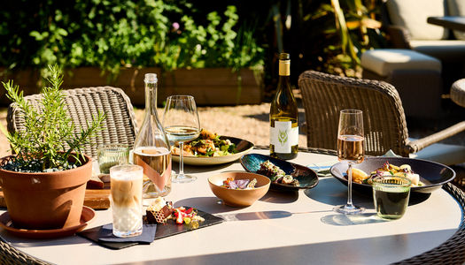 An alfresco summer feast with wine on the terrace with foliage in the background.