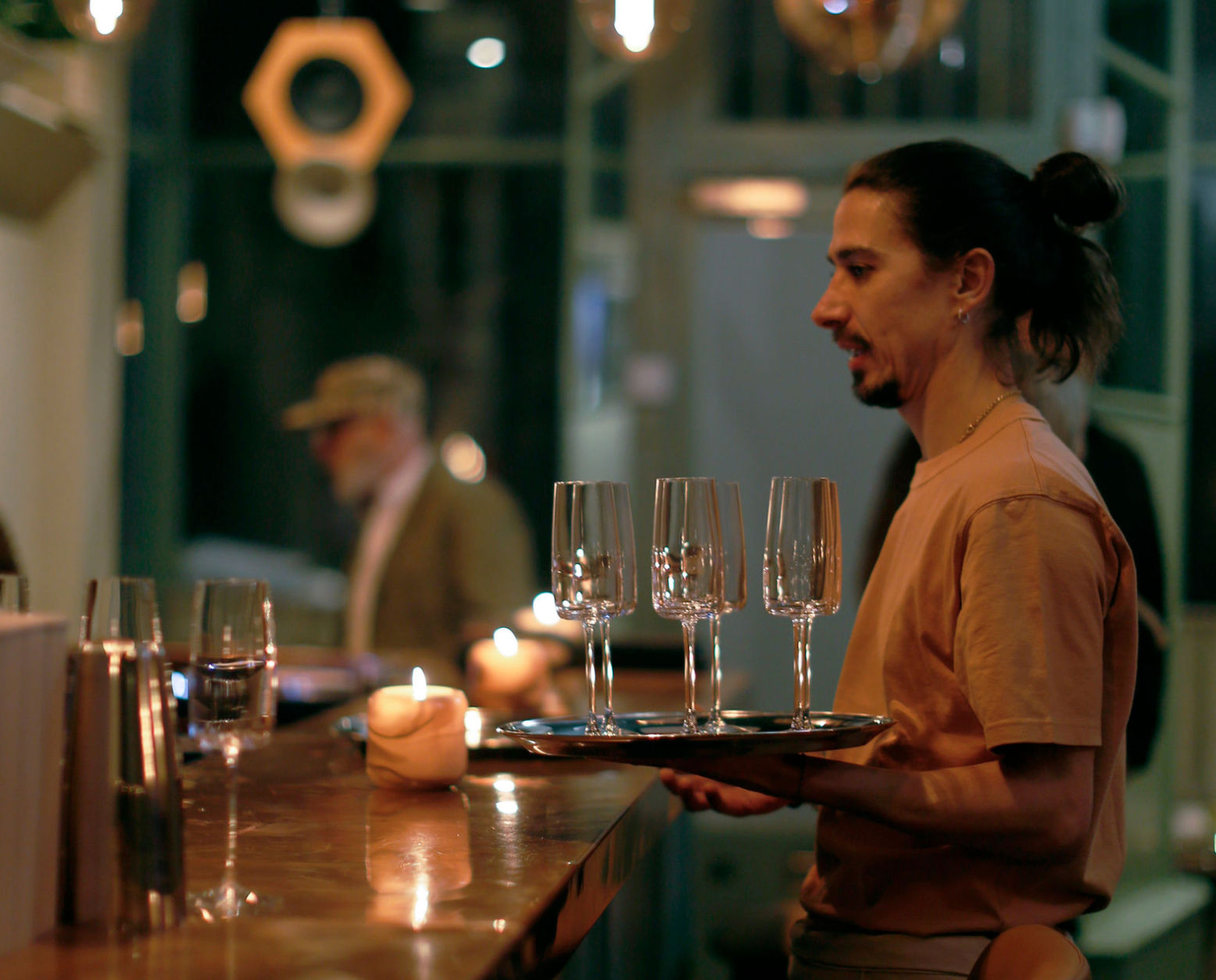 Waiter carrying glasses at Stem. low lit wooden bar with a diner in the background
