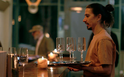 Waiter carrying glasses at Stem. low lit wooden bar with a diner in the background