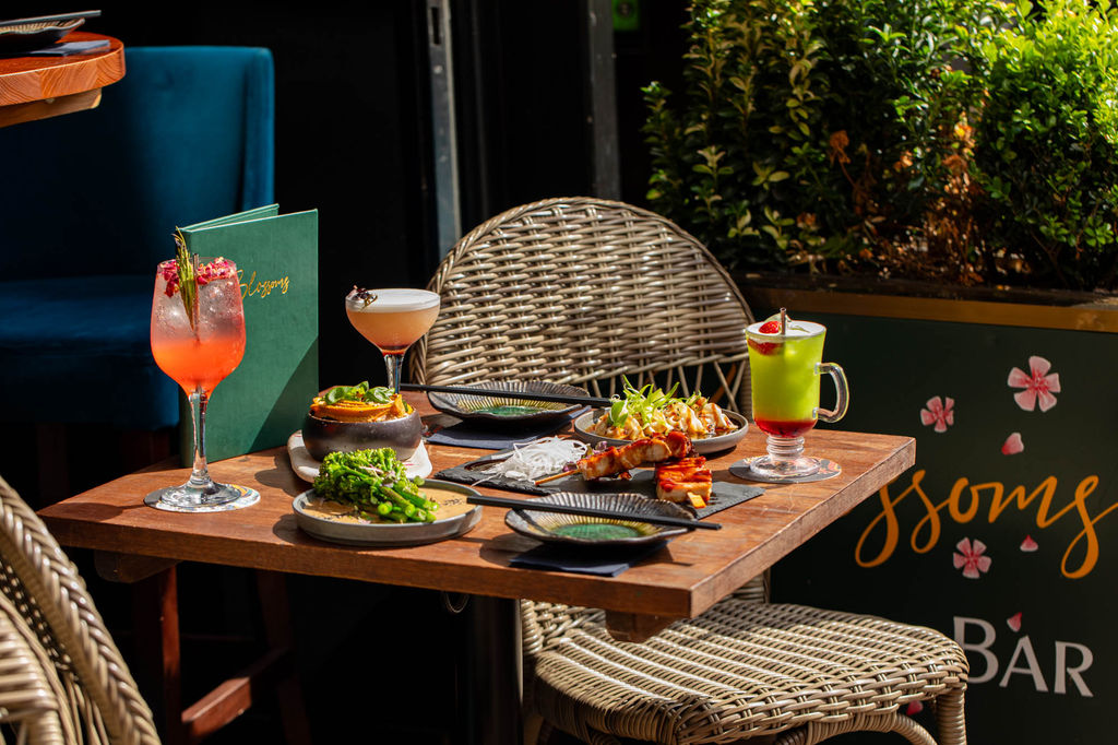 Small plates of food served on a table outside of Blossoms Cocktail Bar on a sunny summer day.