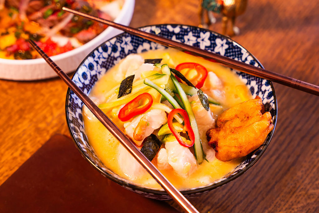A close up of a ceramic floral bowl with a broth-based dish garnished with fresh chillies