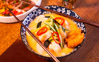 A close up of a ceramic floral bowl with a broth-based dish garnished with fresh chillies