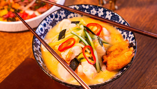 A close up of a ceramic floral bowl with a broth-based dish garnished with fresh chillies