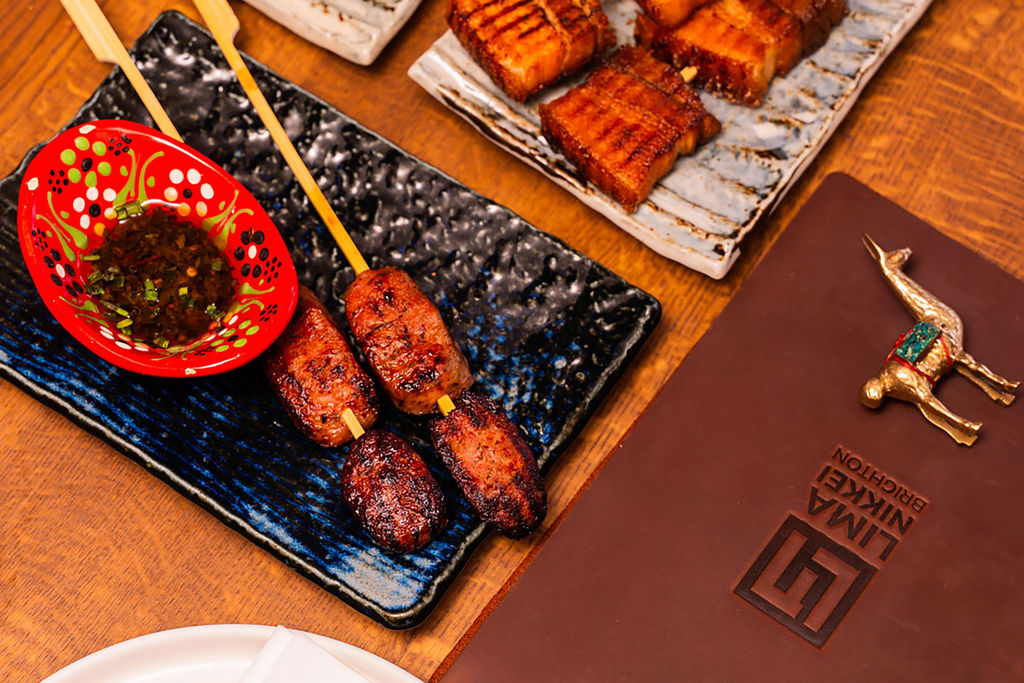 A close up photo of the yakitori skewers on a blue rectangle plate and a small red dish with a dipping sauce