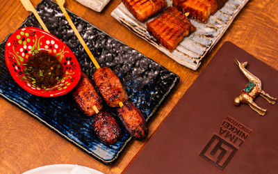 A close up photo of the yakitori skewers on a blue rectangle plate and a small red dish with a dipping sauce