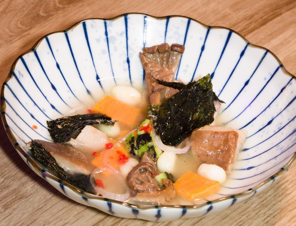 a plate of Nikkei food. Presented in a white blue shell like bowl with seaweed and pork.