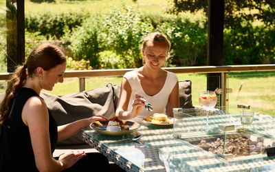 Two women dining alfresco on a summer day eating desserts with a gin and tonic in front of a backdrop of the South Downs.