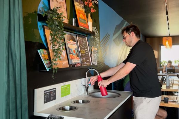 Man filling red bottle at a sink. There are holes in the worktop for recycling and general waste.