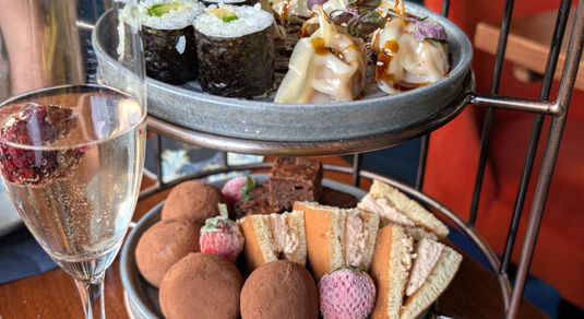 Two tiers of a Japanese tea with sushi and gyoza on the top tier.