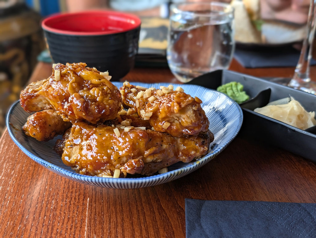 Sticky chicken glazed with sesame seeds and a red and black Japanese tea cup in the background at Blossoms Brighton