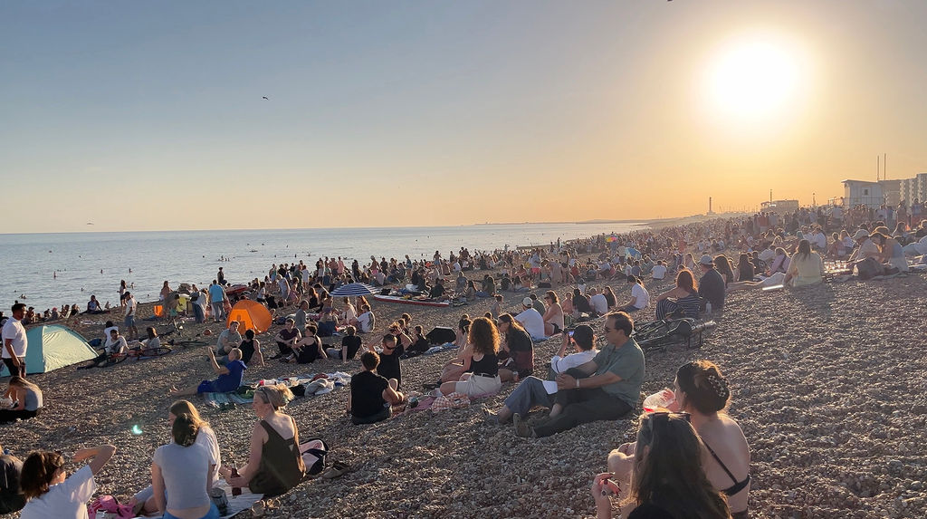 Summer on the beach with a crowd of people sitting on the stones.