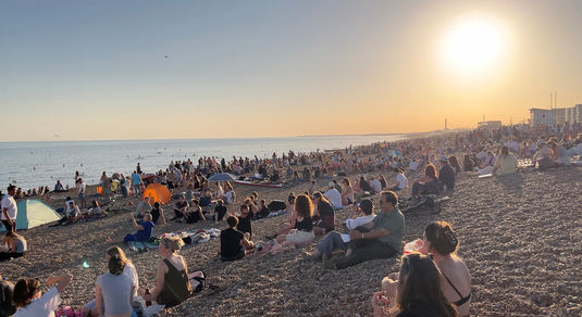 Summer on the beach with a crowd of people sitting on the stones.
