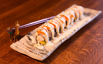 Sushi lined up on a long rectangle ceramic plate with a creamy sauce and chopsticks on the table
