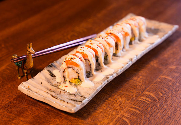 Sushi lined up on a long rectangle ceramic plate with a creamy sauce and chopsticks on the table