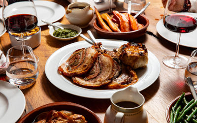 Sunday roast laid out on a table with glasses of red wine and a plate in the middle of the table with sliced meat.