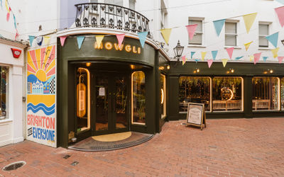 Green painted facade of Indian street food restaurants in The Lanes with bunting in the street and a lit up Mowgli sign.