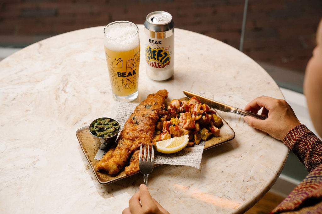 A table with a rectangle plate of Mowgli fish and chips alongside a pint of beer