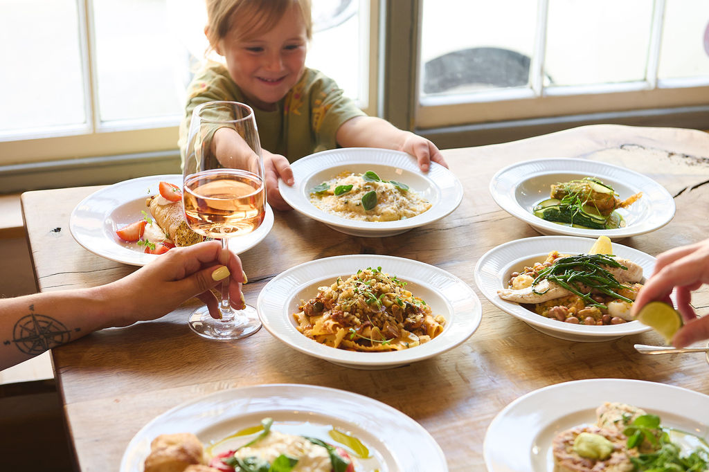 A chile reaching for a bowl of pasta at a table looking happy