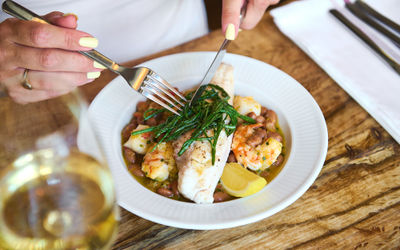 Fish with samphire and a person holding a knife and fork cutting into the fish